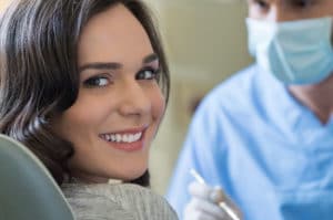 Young woman with bright white teeth smiling while a dentist inspects her teeth