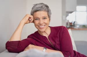 Portrait of smiling senior woman relaxing on couch at home. Happy mature woman sitting on sofa and looking at camera. Closeup of lady relaxing at home.