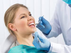 Blonde woman in dental chair smiles brightly after receiving a realistic-looking dental implant.