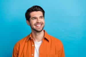 Attractive brunette man in orange shirt has a nice smile after dental implant placement.
